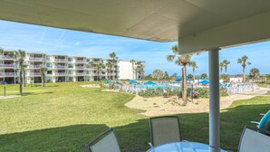 En hotelgård med poolområde, palmer og en overdækket siddeplads.