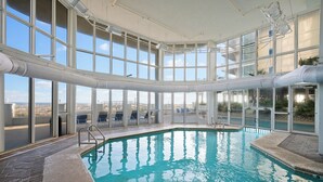 An indoor swimming pool with clear glass walls, a tiled floor, and a view of the cityscape. - NEW RENTAL-Oceania 13-Luxury 4000 SQ FT Gulf Front Condo-Signature Properties (Gulf Shores)