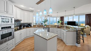 A modern kitchen with white cabinetry, granite countertops, and a central island. - NEW RENTAL-Oceania 13-Luxury 4000 SQ FT Gulf Front Condo-Signature Properties (Gulf Shores)