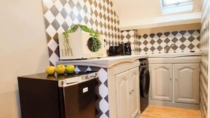 A compact kitchen with a black refrigerator, a microwave, and a coffee maker on the counter. There are three apples on the refrigerator. The kitchen has a patterned backsplash and wooden flooring. - Studio Design - Unique - Centre Ville (Bagnères-de-Bigorre)