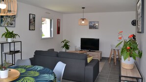 Un salon moderne avec un canapé gris, une table basse en bois, un téléviseur et des plantes en pot.