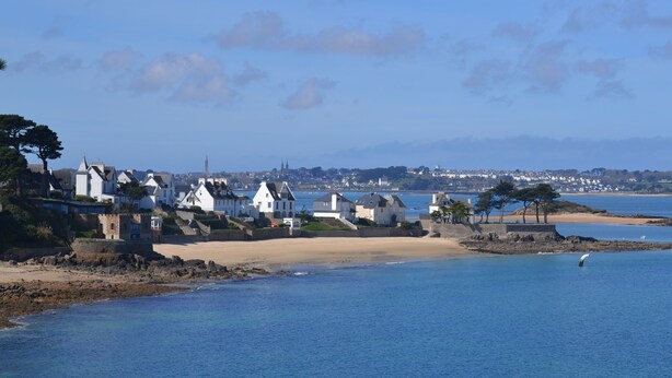 Une ville côtière aux maisons blanches, avec une plage de sable fin et une mer d’un bleu limpide.