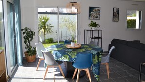 Un coin repas avec une table dressée pour quatre personnes, entourée de chaises, d’un canapé et de plantes en pot.