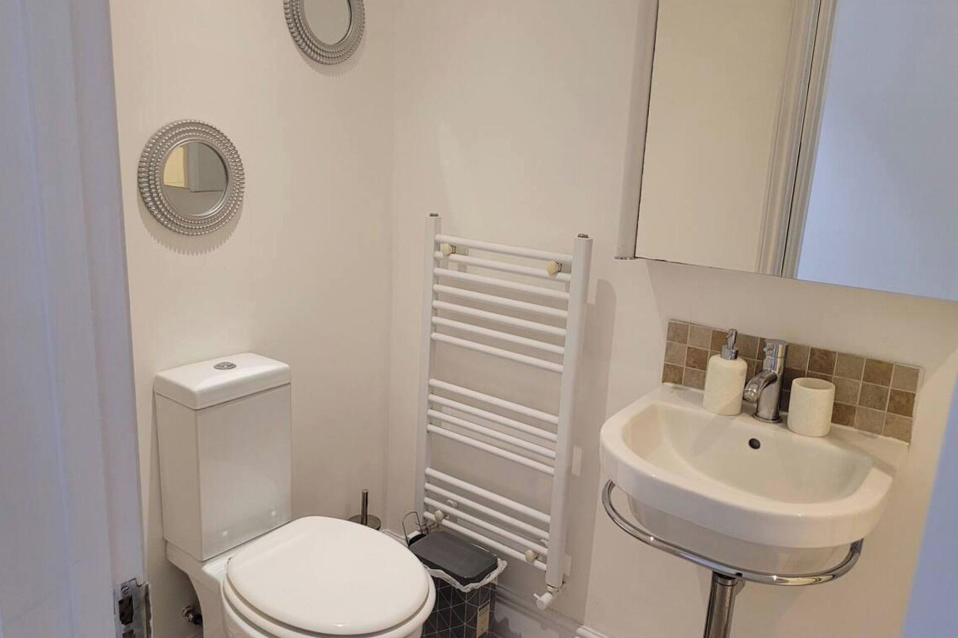 A small, clean bathroom with a toilet, a sink, a towel rack, and two mirrors.