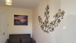 A living room with a sofa, a wall-mounted decorative metal piece, and a framed landscape painting. - Apartment - Sleeps 2 - Parking - Wi-fi (Reading)