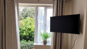 A room with a TV mounted on the wall, a window with curtains, and a potted plant on the windowsill. - Apartment - Sleeps 2 - Parking - Wi-fi (Reading)