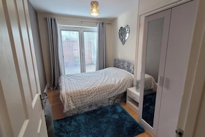 Un dormitorio con cama, armario, mesita de noche y ventana con cortinas.