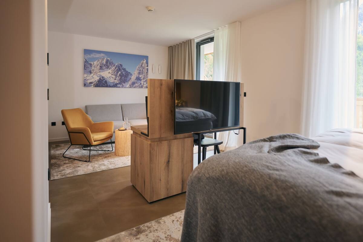 Een moderne hotelkamer met een bed, een televisie, een houten bureau, een stoel en een schilderij aan de muur.