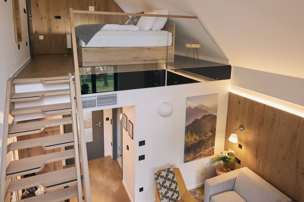 Een slaapkamer in loftstijl met een stapelbed, een trap, een eethoek en een zithoek met een bank en salontafel.