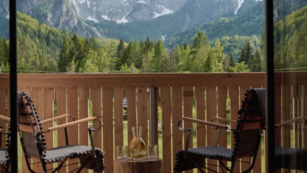 Ein Balkon mit zwei Stühlen und einem Holztisch, mit Blick auf eine Berglandschaft.