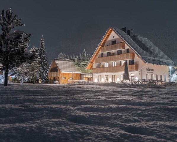 Un grand bâtiment à plusieurs étages, doté d’un toit en pente, qui ressemble probablement à un hôtel ou à un complexe touristique, entouré d’arbres couverts de neige et d’un paysage hivernal.