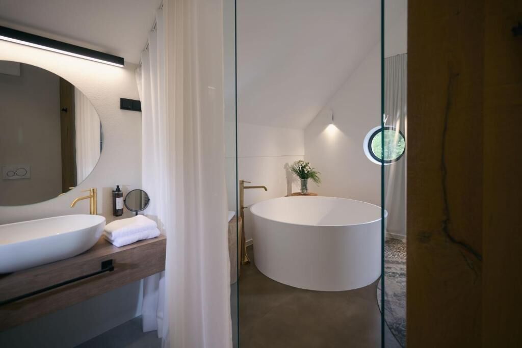 Ein modernes Badezimmer mit einer großen, ovalen Badewanne, einem runden Spiegel und einem hölzernen Waschtisch.