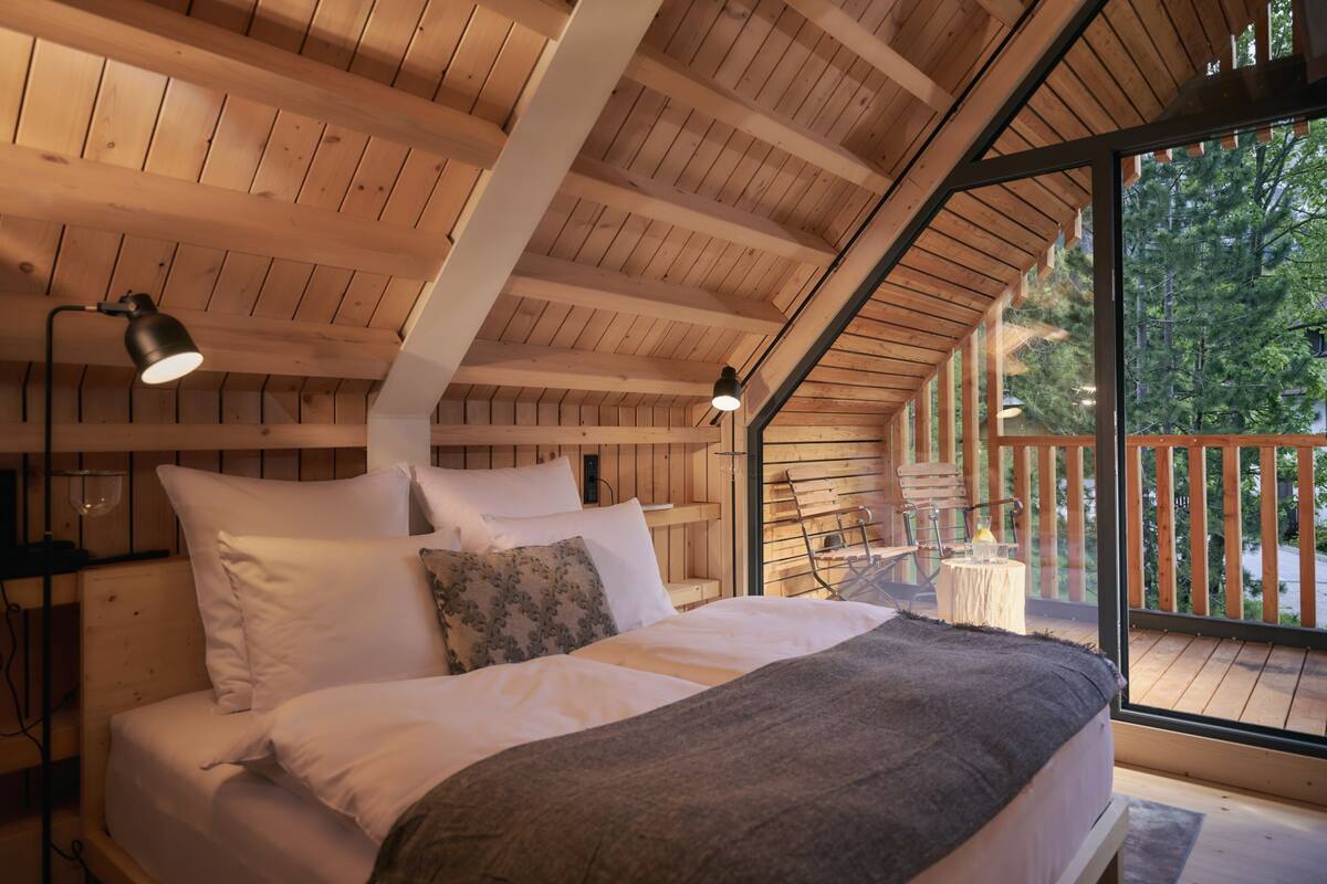 Een slaapkamer in een houten blokhut met een bed, kussens en een nachtkastje.
