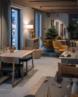 Un espace de repas moderne avec une longue table et des chaises, une petite table d’appoint avec une lampe et un sapin de Noël.