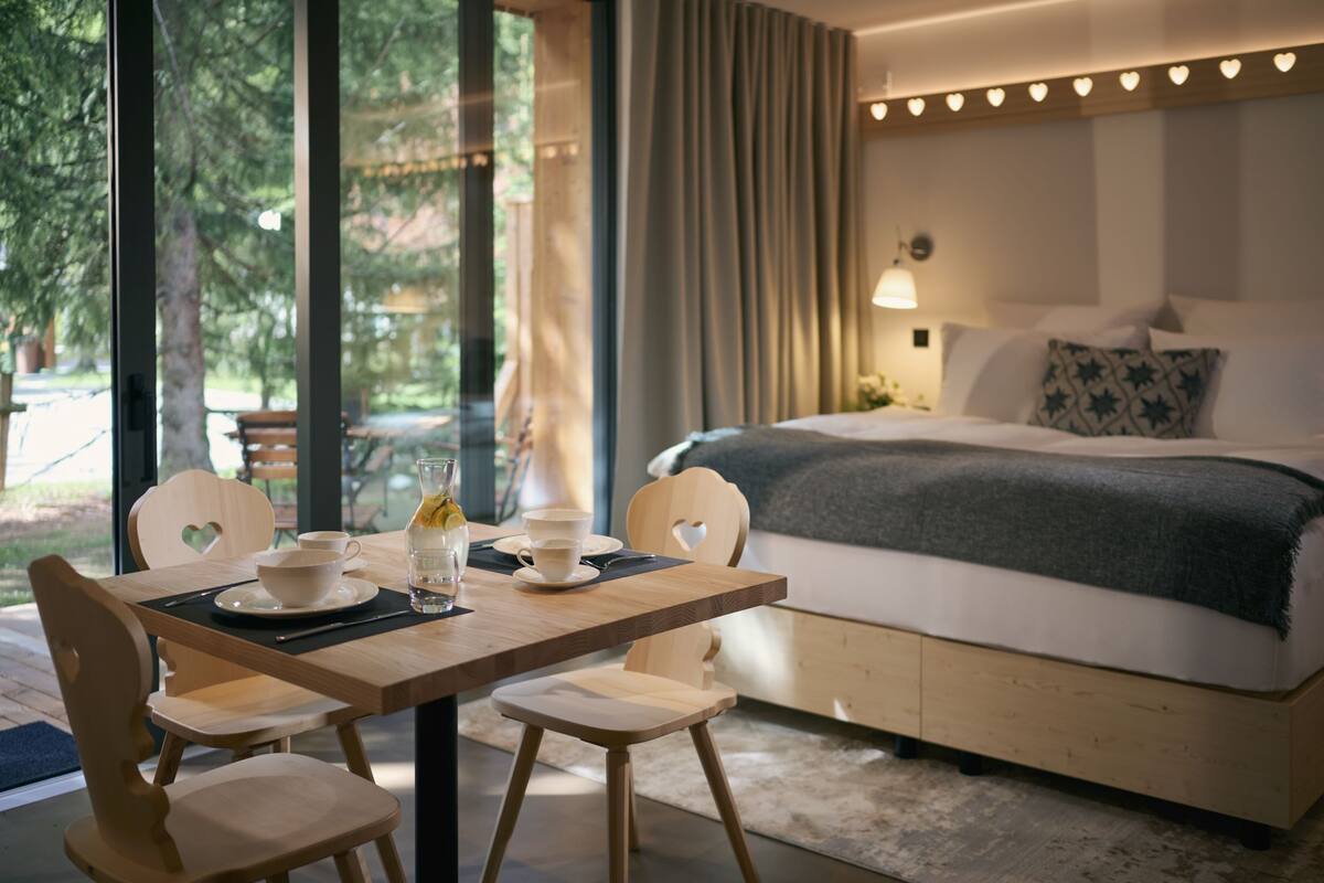Een moderne slaapkamer met een groot bed, een houten tafel met stoelen en uitzicht op de omgeving.