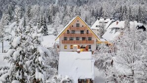 Eine Berghütte mit Holzfassade, umgeben von schneebedeckten Bäumen und Bergen.
