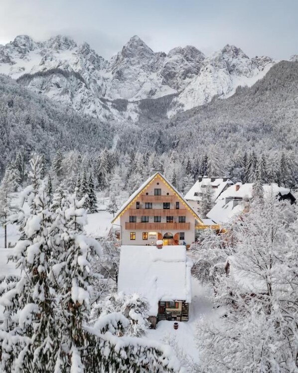 Un chalet de montagne à la façade en bois, entouré d’arbres et de montagnes couverts de neige.