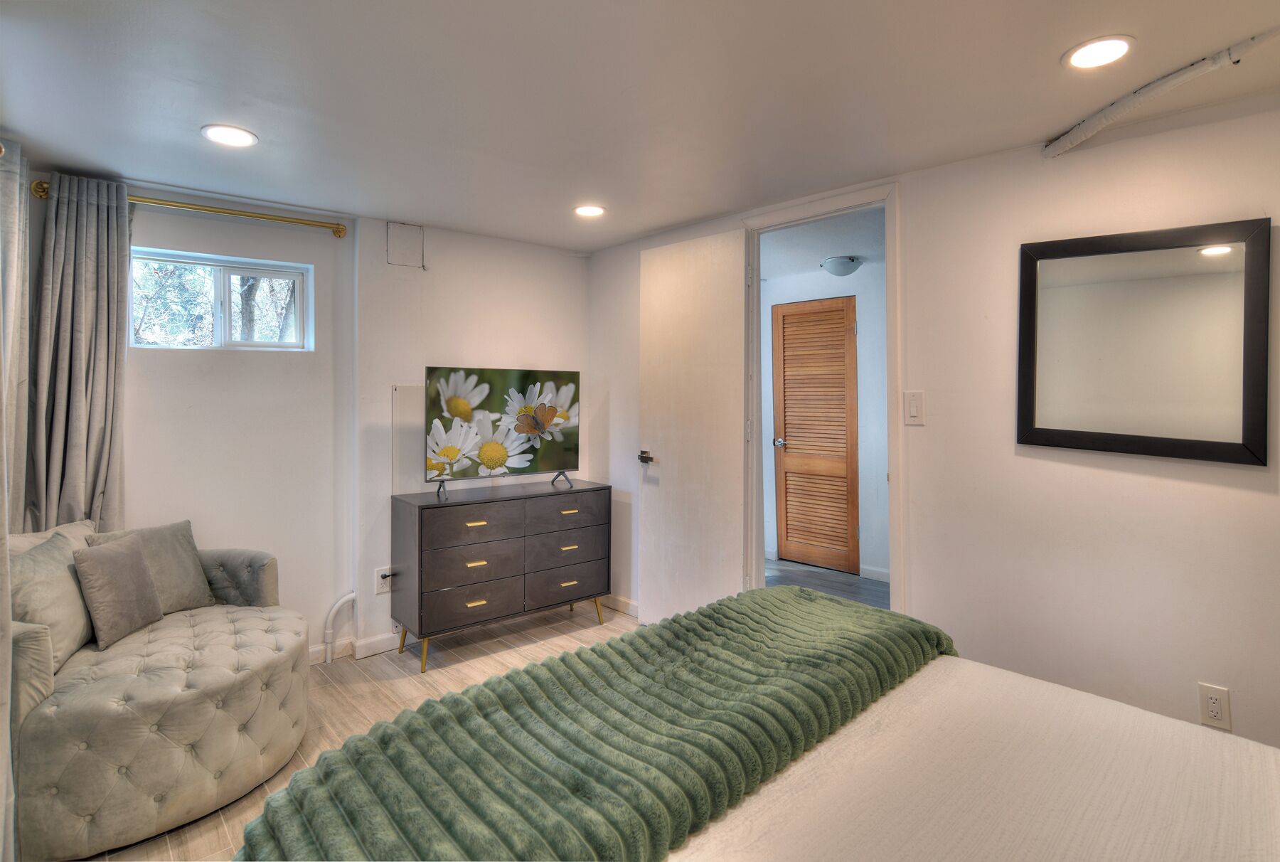 A bedroom with a bed, a dresser, a mirror, and a window with curtains.