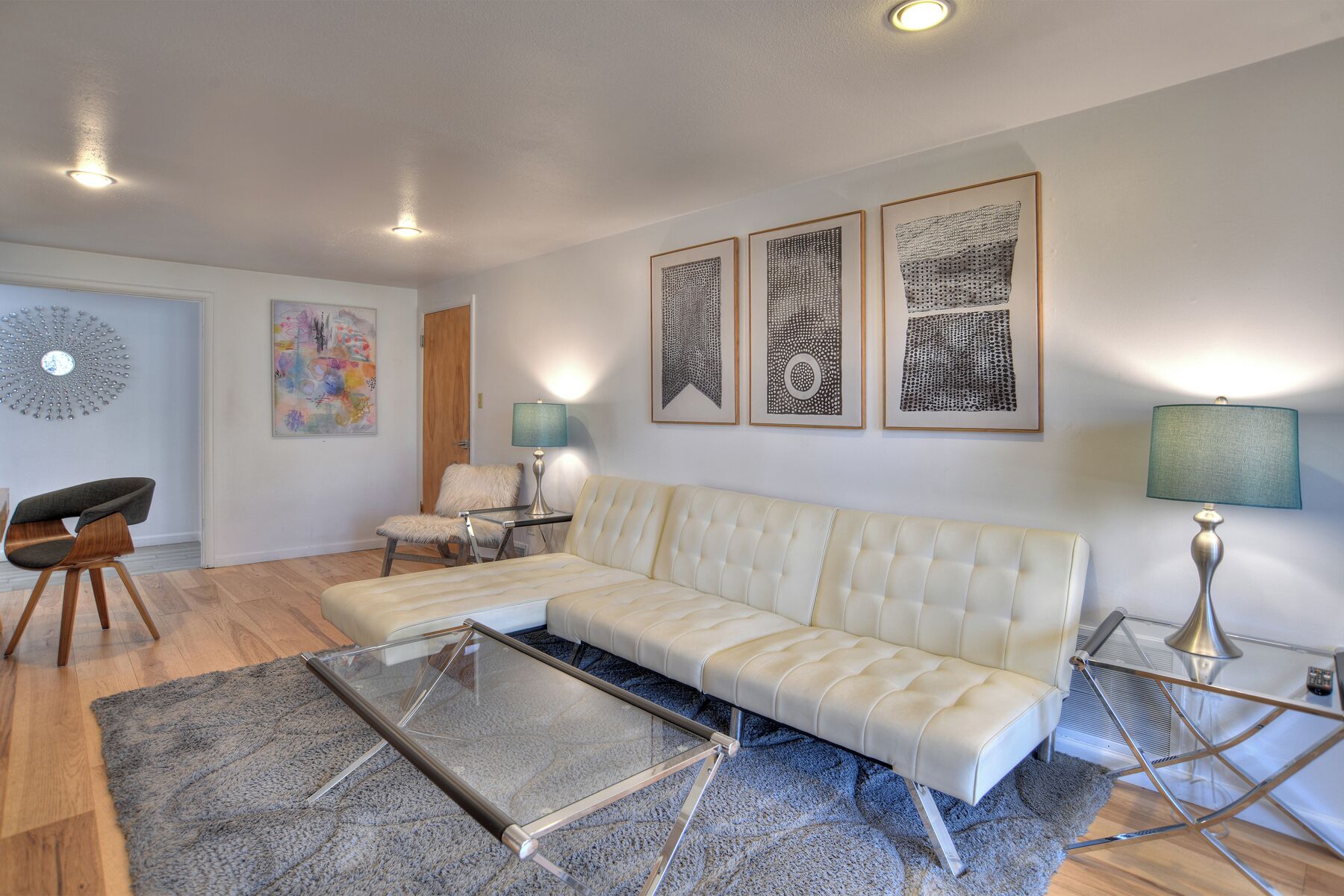 A modern living room with a sectional sofa, a glass coffee table, a fluffy rug, and framed artwork on the wall.