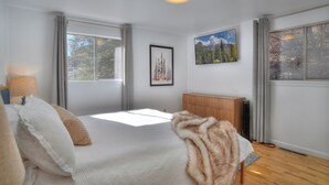 A modern bedroom with a large bed, a wooden dresser, and two windows offering views of trees and mountains. - Mid Century Mountain Home on 3 acres - 10 Minutes to DGO - AC-Hot Tub-Views (Durango)