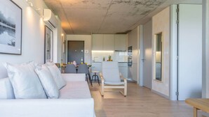 A modern living room with a sofa, a dining area with a table and chairs, and a kitchen in the background. - Luxurious Soft Flat | Balcony and Pool by HostWise (Vila Nova de Gaia)