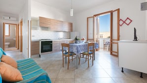 A modern kitchen with wooden cabinets, a dining table with chairs, and a kitchenette. - 3209 Complesso Pergolesi - Appartamento DX by Barbarhouse (Melendugno)