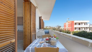 A balcony with a table set for dining, wooden shutters, and a view of buildings in the background. - 3209 Complesso Pergolesi - Appartamento DX by Barbarhouse (Melendugno)