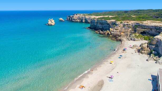 A coastal beach with clear turquoise waters, rocky cliffs, and a sandy shore with umbrellas and beachgoers. - 3209 Complesso Pergolesi - Appartamento DX by Barbarhouse (Melendugno)