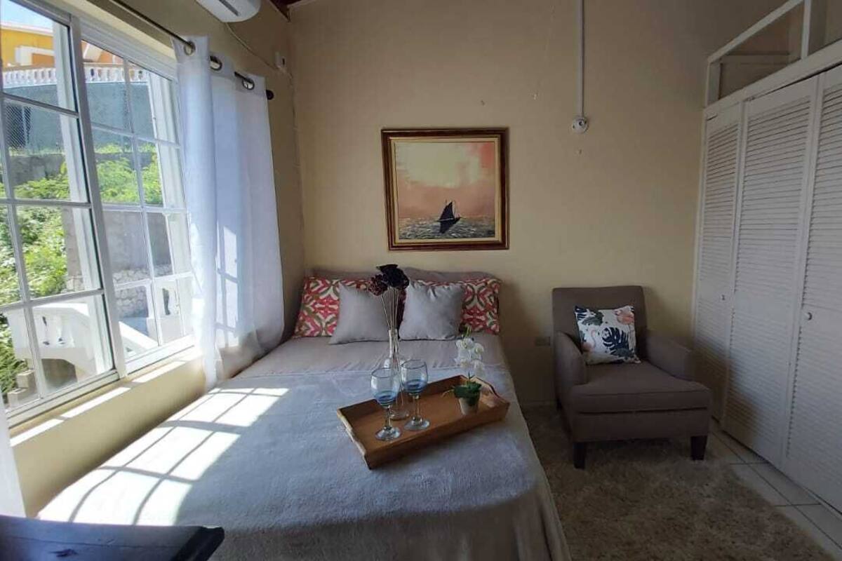 A bedroom with a bed, a chair, a window, a painting, and a wardrobe.