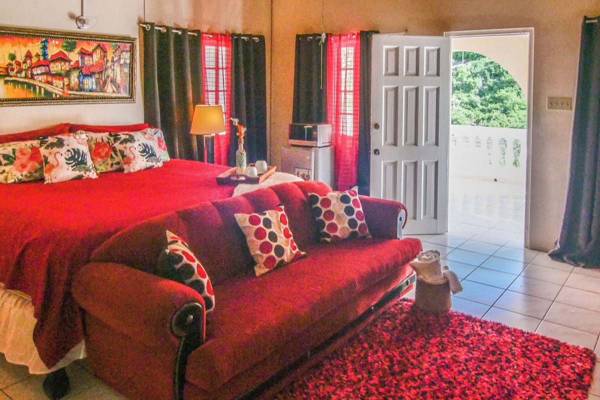 A bedroom with a large bed, a sofa, a lamp, and a painting on the wall.