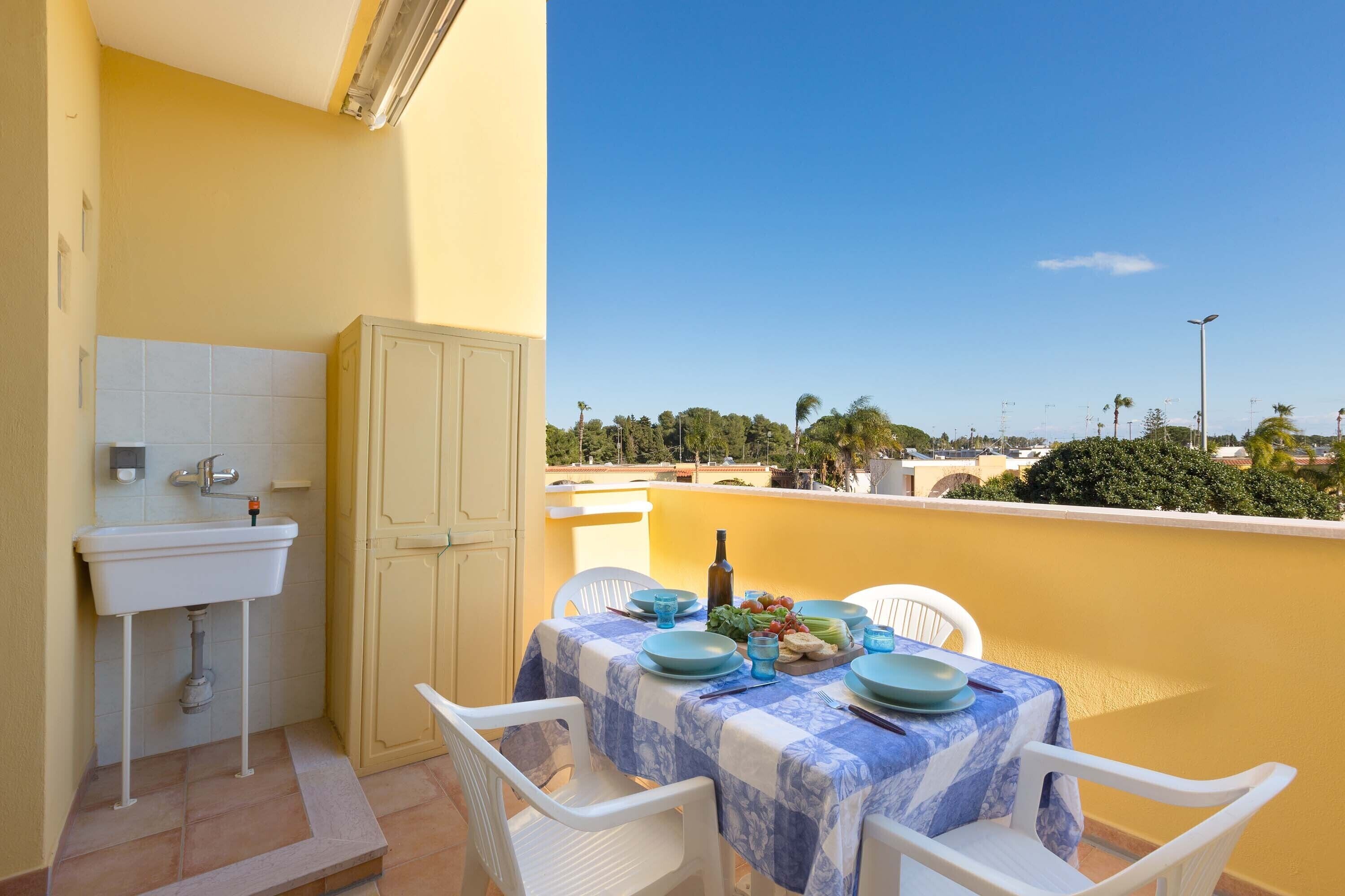 Un balcon avec une table dressée pour deux personnes, un évier et une porte.