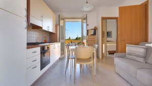 A modern kitchen with white cabinets, a dining area with a table and chairs, and a living room with a sofa and a TV. - 3198 Marajò House by Barbarhouse (Melendugno)
