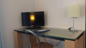 A small office space with a desk, a chair, a computer monitor, a keyboard, a lamp, and some binders.