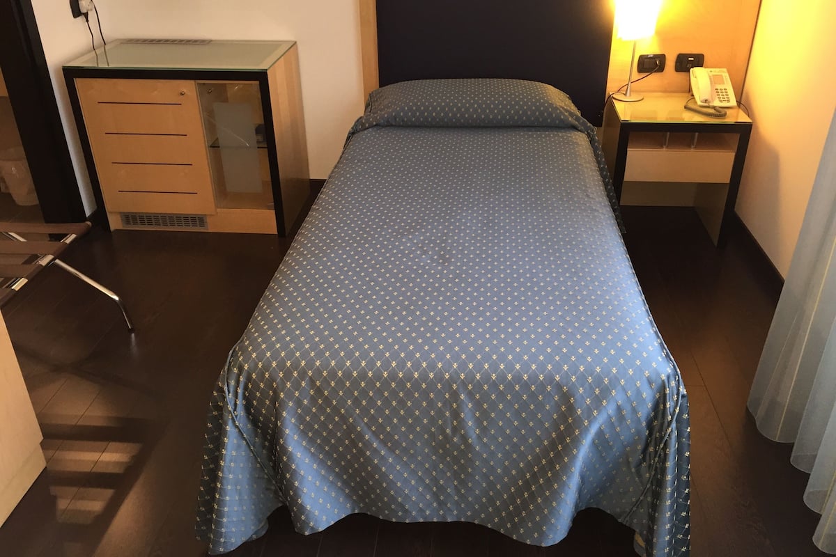 Une chambre d’hôtel avec un lit, un bureau, une chaise, une lampe et un téléphone sur la table de chevet.