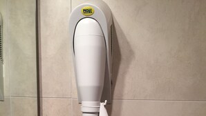 Un termosifone portatile bianco con tubo flessibile, fissato a una parete rivestita di piastrelle.