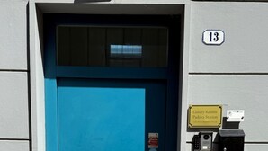 Una porta blu con un cartello con il numero 13 sopra, che indica il numero di una stanza. C'è un'insegna per 'Luxury Rooms Padova Station' e una telecamera di sicurezza montata al muro.