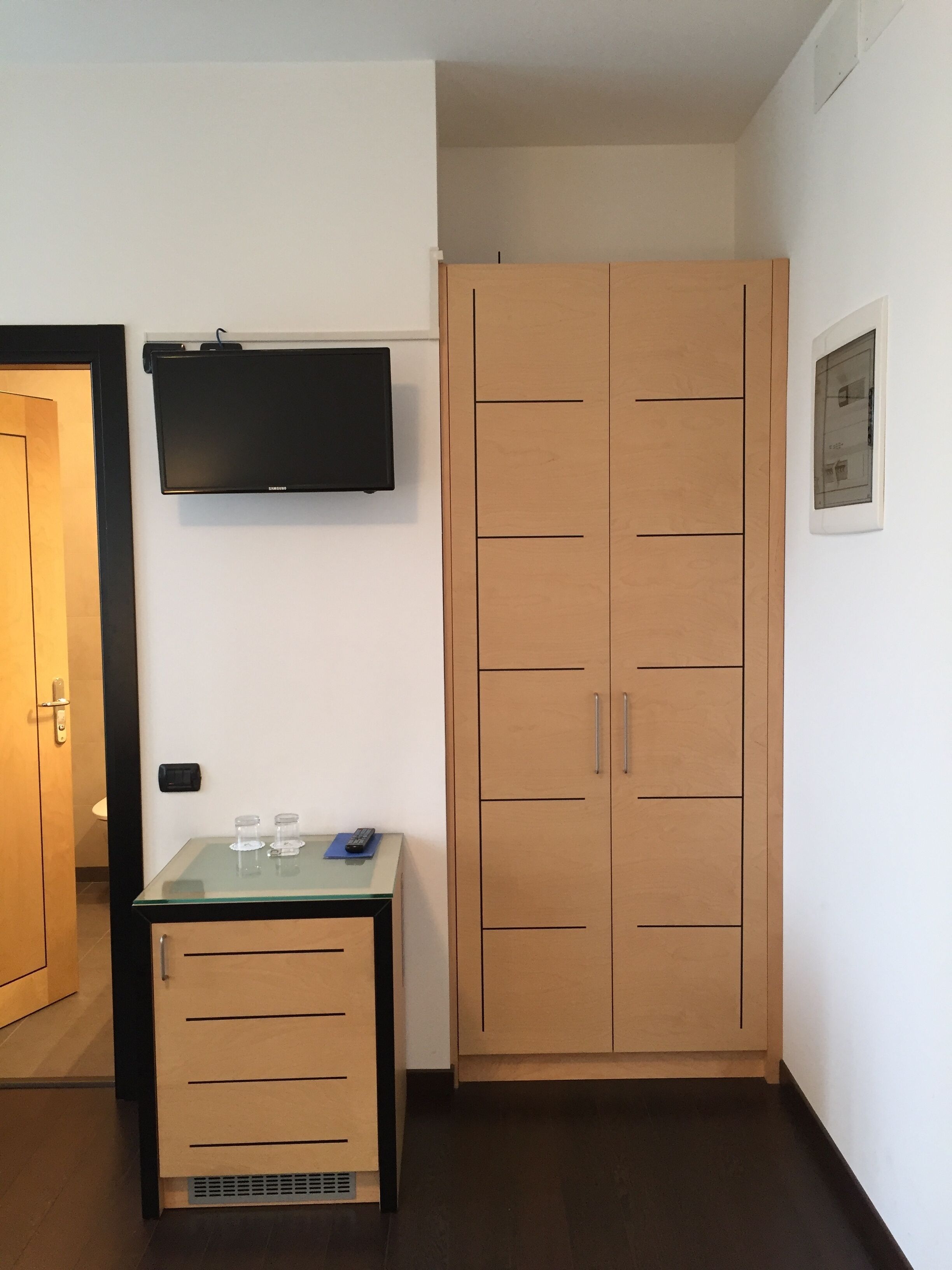 Quarto com guarda-roupa de madeira, uma mesa pequena com um controle remoto e televisão na parede.