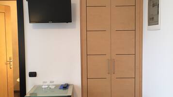 Ein Zimmer mit einem Holzschrank, einem kleinen Tisch mit Fernbedienung und einem an der Wand montierten Fernseher.