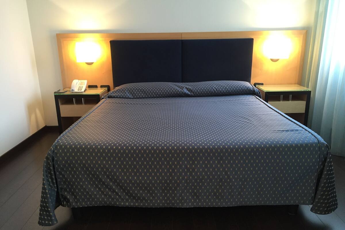 Une chambre d’hôtel avec un grand lit, deux tables de chevet, un téléphone et des lampes fixées au mur.
