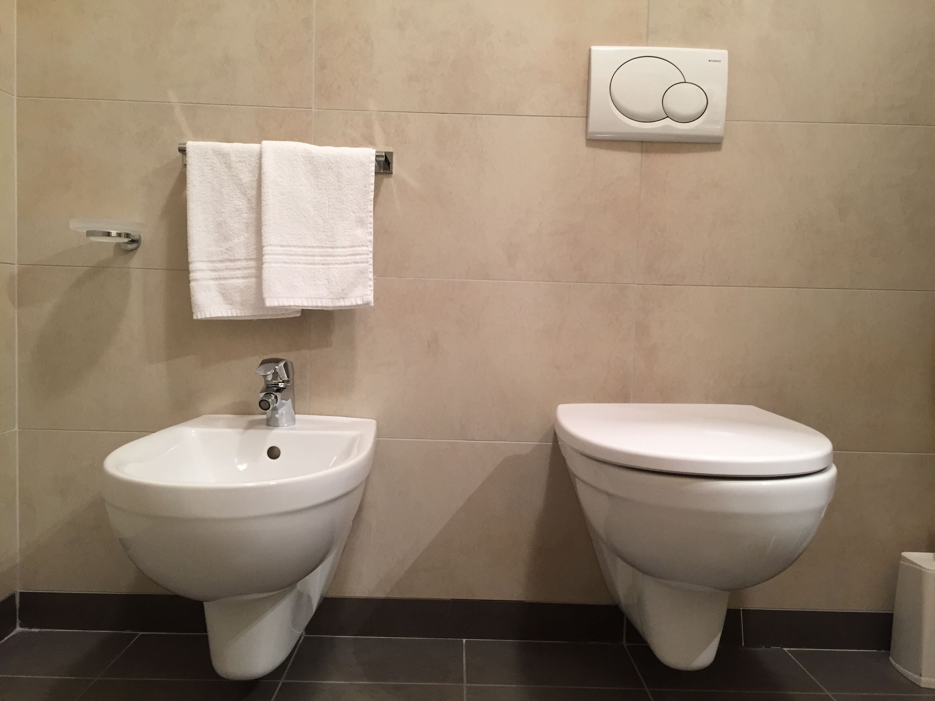 A bathroom with two toilets, a sink, and a towel rack.