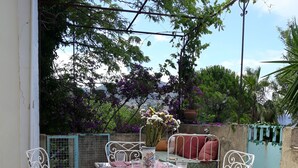 A patio with a white metal table and chairs, surrounded by greenery and a view of mountains.