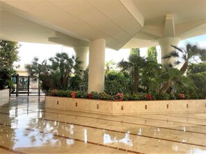 A spacious indoor area with a polished floor, large columns, and a variety of plants including palm trees and flowering shrubs. - (103) Le palm beach à porté (Cannes)