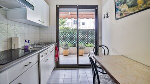 Una cuina compacta amb zona de menjador, una porta corredissa de vidre que dona a un balcó amb plantes en testos i un quadre a la paret.
