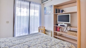 Un dormitori amb un llit, una televisió sobre una estant i una finestra amb cortines.