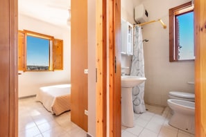 A bedroom with a bed and a window, a bathroom with a sink and toilet, and a view of the sea through a window. - 3210 Complesso Pergolesi - Appartamento SN by Barbarhouse (Melendugno)