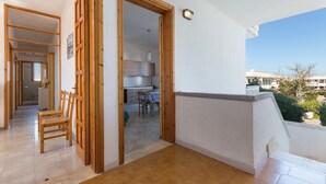 A balcony with a wooden floor, a white wall, and a view of a building and trees.
