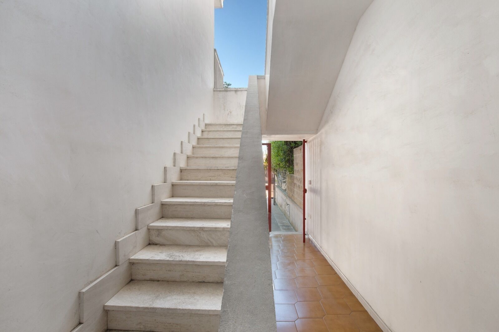 A narrow, white-walled corridor with a staircase leading to an upper level.