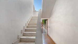A narrow, white-walled corridor with a staircase leading to an upper level.