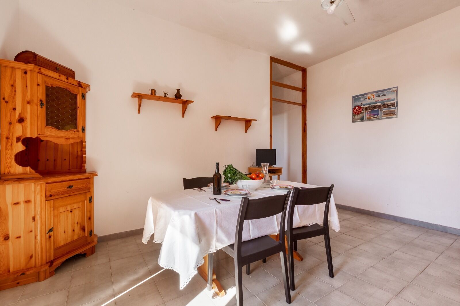 A dining area with a wooden cabinet, a table set for two, and a television on a stand.