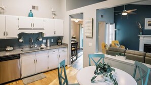 A modern kitchen with white cabinets and a blue backsplash, a dining area with a round table and chairs, and a living room with a sofa and a fireplace. - Family & Pet Friendly Home in Quiet Neighborhood - Close to Beaches & Downtown! (Mount Pleasant)